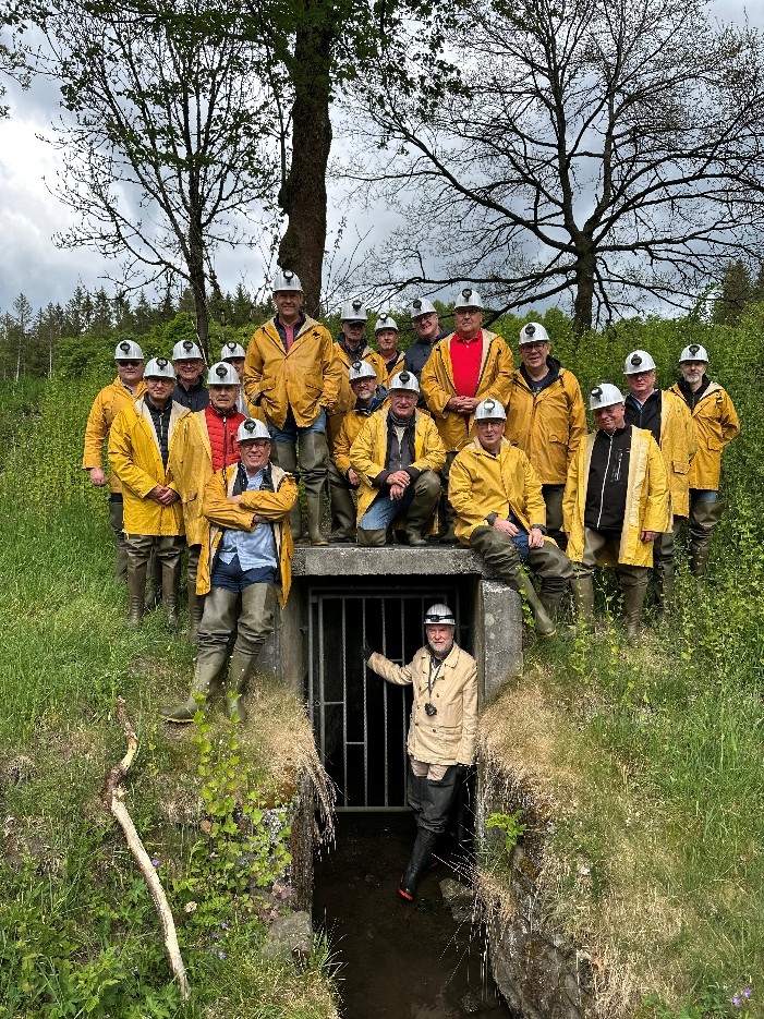 Gruppenfoto von Teilnehmern der Bezirksgruppe Garzweiler in gelben Jacken und Grubenhelmen vor dem Eingang eines historischen Stollens im Grünen